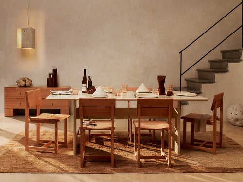 Comedor cálido con mesa y sillas de Ferm Living en madera natural, lámpara colgante y ambiente acogedor.